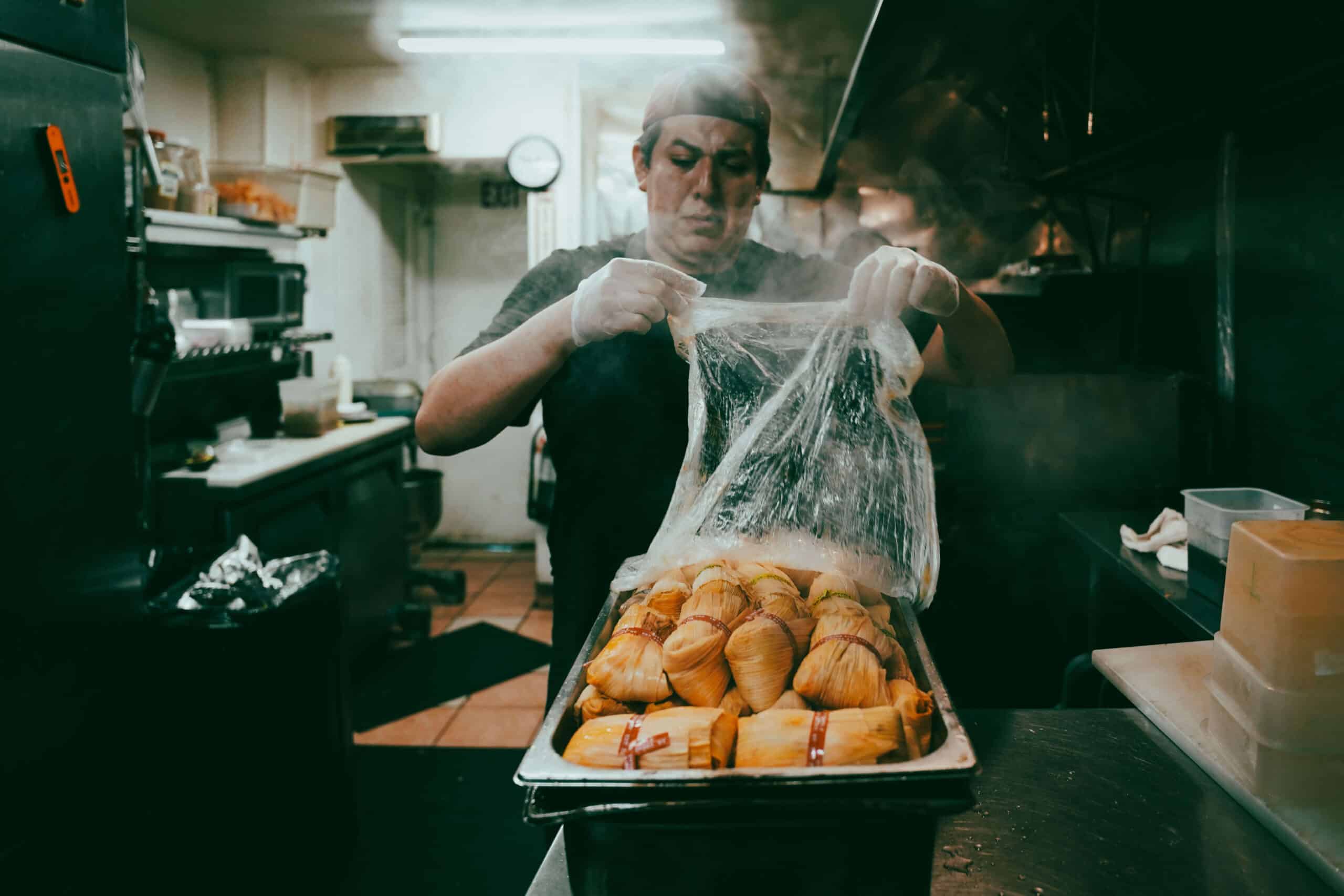 Isrrael Veliz standing in the City Tamale kitchen behind a steaming tray of tamales